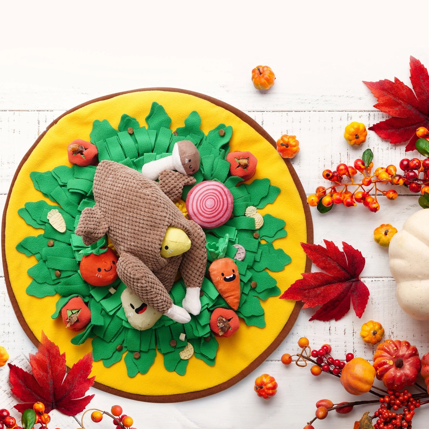 The Nocciola Colorful Turkey-Themed Dog Toys sit on a round yellow and green mat with plush veggies and leaves, surrounded by autumn leaves, berries, and a white pumpkin—ideal for puppies and small breeds.