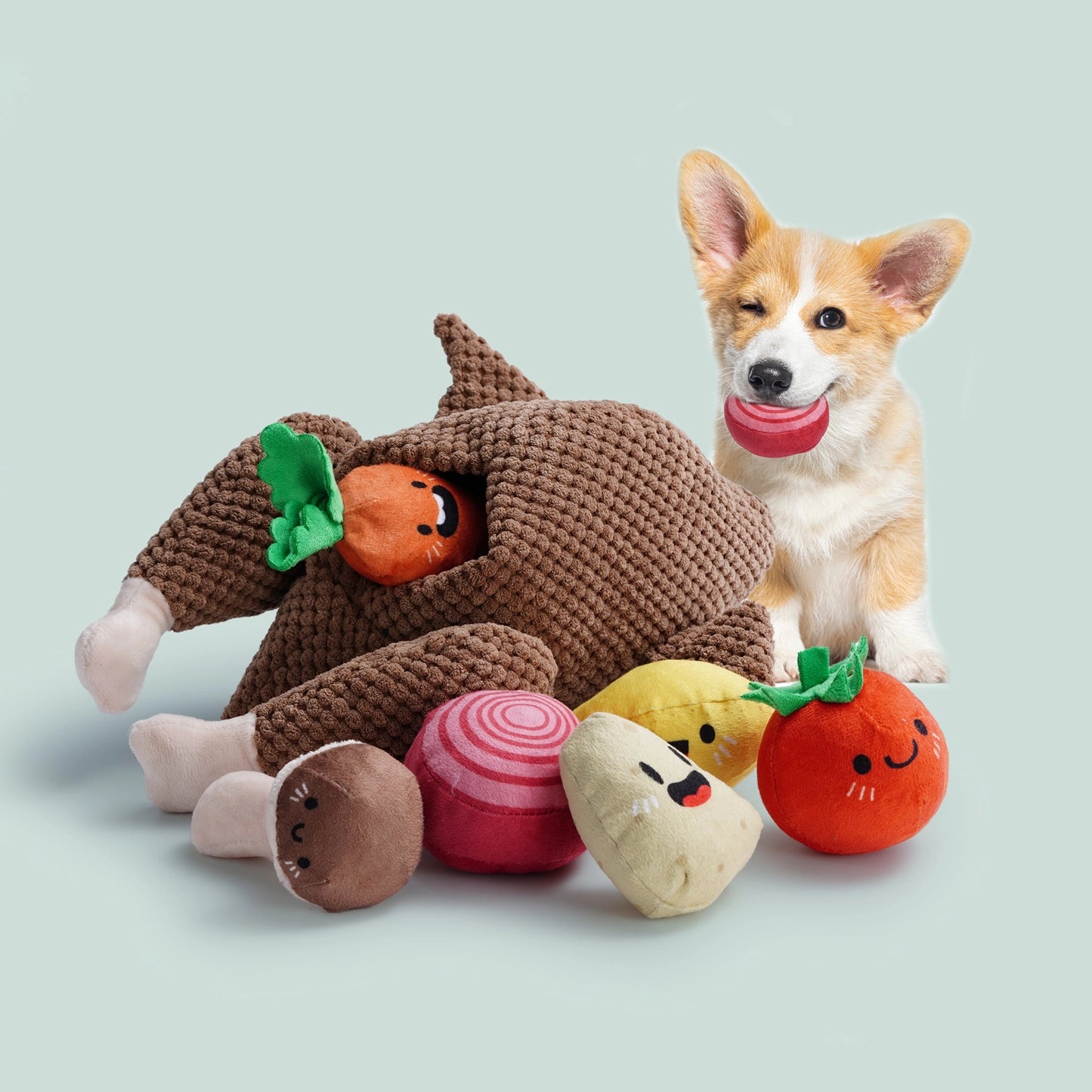 A small dog with a red ball sits behind Nocciola Colorful Turkey-Themed Dog Toys and several vegetable-shaped toys, perfect for puppies and small breeds, on a light green background.