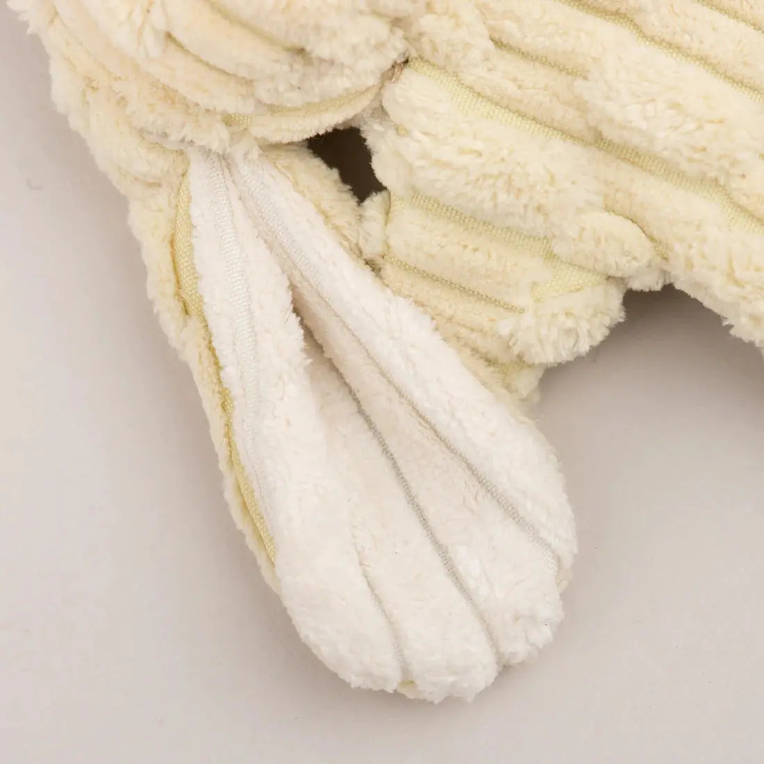Close-up of a cream-colored HuggleHounds Woodland HuggleFlatties Tough Squeaky Plush Small Dog Toy with ribbed fabric and long floppy ears, from the 3-pack set, lying on a light surface.