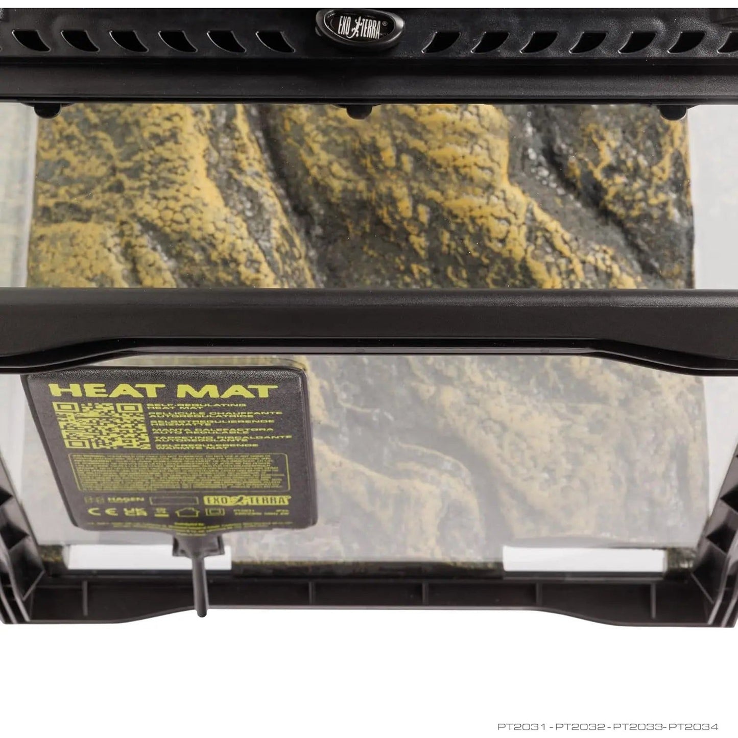 Top view of an empty terrarium with a black lid, featuring an Exo Terra Self-Regulating Heat Mat for Reptiles & Amphibians attached to the ceiling and a rocky floor. The heat mat’s label is visible through the glass.