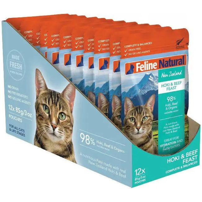 A display box of Feline Natural Feast Grain-Free Wet Cat Food Pouch 12/3oz by Feline Natural, featuring a tabby cat, mountain scenery, and product details. Contains 12 orange and blue 3oz pouches for cats.