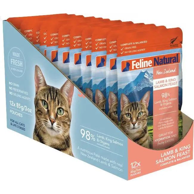The Feline Natural Feast Grain-Free Wet Cat Food Pouch 12/3oz retail box features a tabby cat, mountains, and highlights 98% grass-fed lamb meat with no grains or preservatives. Brand: Feline Natural.