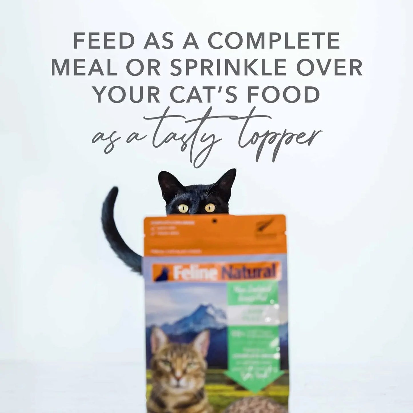 A black cat peeks over a bag of Feline Natural New Zealand Beef & Hoki Feast Grain-Free Freeze-Dried Cat Food. Text above reads: Feed as a complete meal or use as a delicious topper for your cat’s food.