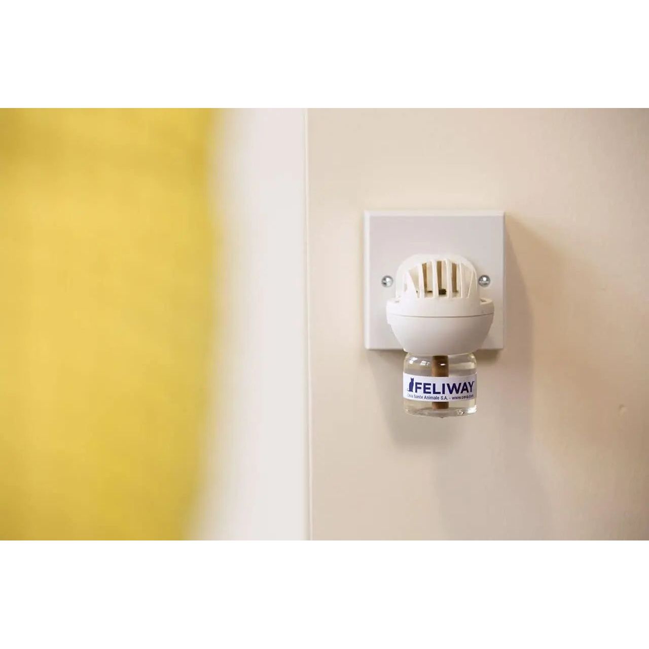 A Feliway Classic Cat Calming Pheromone 30 Day Refill by Feliway in a diffuser plugged into a wall, releasing calming pheromones to reduce cat stress. The background shows a yellow blurred area on the left side.