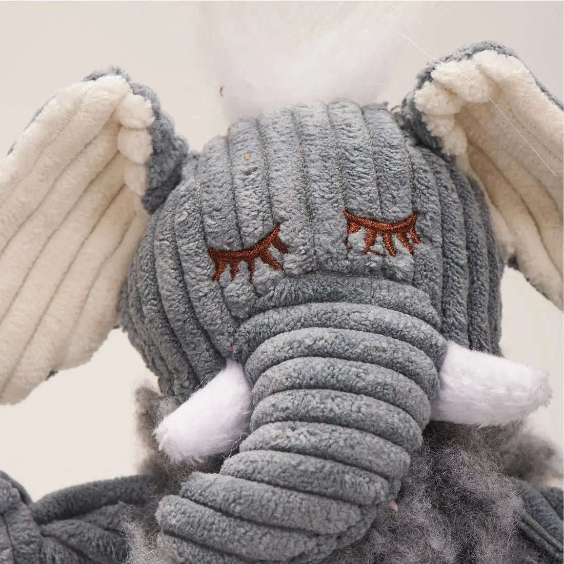 Close-up of the HuggleHounds Ellamae Elephant HuggleFleece FlufferKnottie Plush Dog Toy—a gray, corduroy-textured, washable toy with embroidered eyes, white tusks, floppy cream-lined ears, and a tuft of white hair.