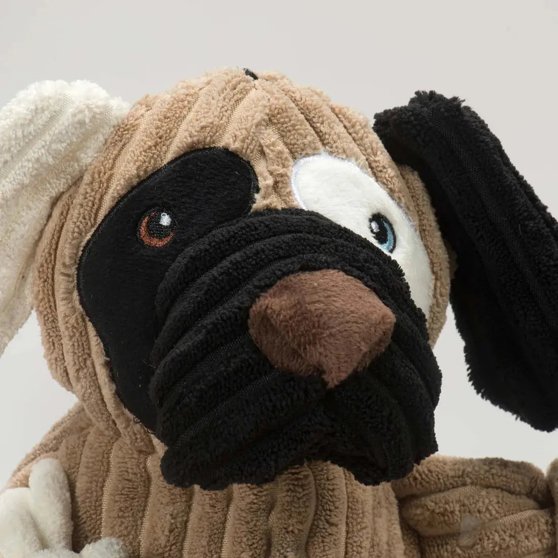 Close-up of the HuggleHounds Huggle Mutts Patches the Mutt Tough Squeaky Plush Dog Toy, featuring durable corduroy fabric, a beige body, black ears, brown nose, and a big black eye patch with a cute cartoon face.