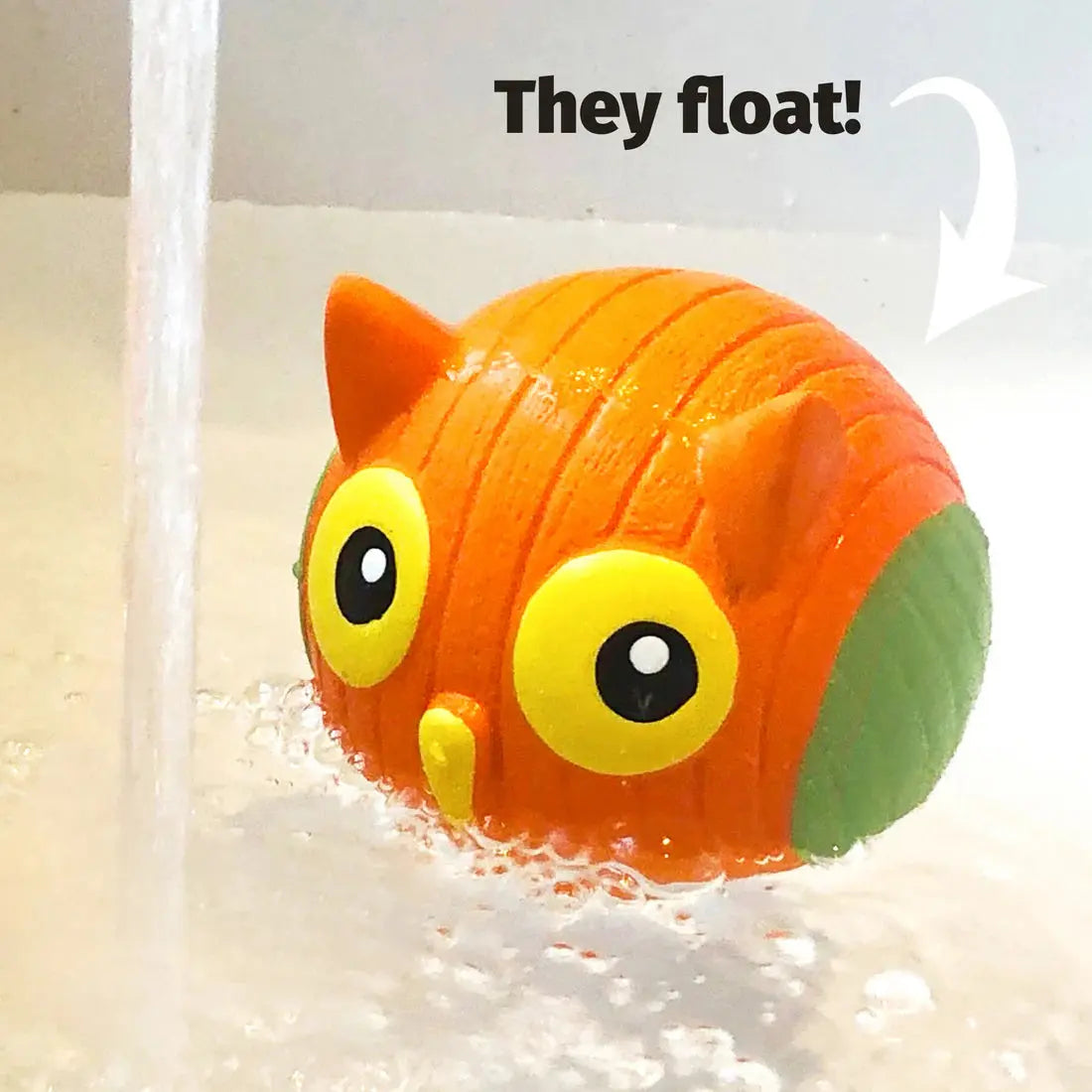 The HuggleHounds Ruff-Tex Squeaky Ball Dog Toy by HuggleHounds, shaped like an orange owl with big yellow eyes, floats in bubbly water—perfect for playful pups who love bath time. Above it reads, They float! with an arrow pointing to the toy.