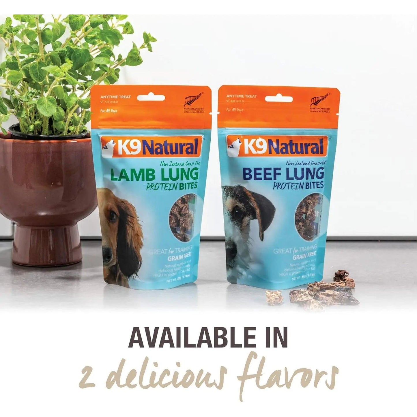Two bags of K9 Natural Protein Bites—Lamb Lung and Beef Lung Protein Bites Air-Dried Dog Treats 2.1oz by K9 Natural—are on a counter next to a potted plant. Text below reads: Available in 2 delicious flavors.