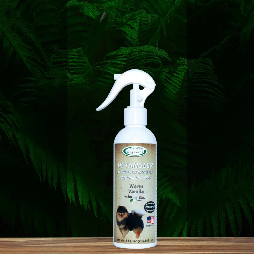 An 8oz bottle of Mad About Organics Detangler Spray—Knot-Free Coats Made Easy—with a deodorizing cedarwood scent, dog on the label, and trigger nozzle is displayed against a dark green fern background.