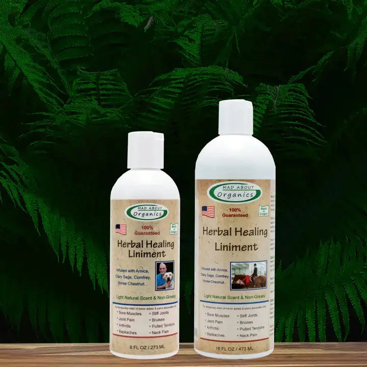Two bottles of Mad About Organics Herbal Relief Liniment, in 8 fl oz and 16 fl oz sizes, are shown before green ferns. The beige labels emphasize Arnica and other natural ingredients for gentle, effective relief. Brand: Mad About Organics.