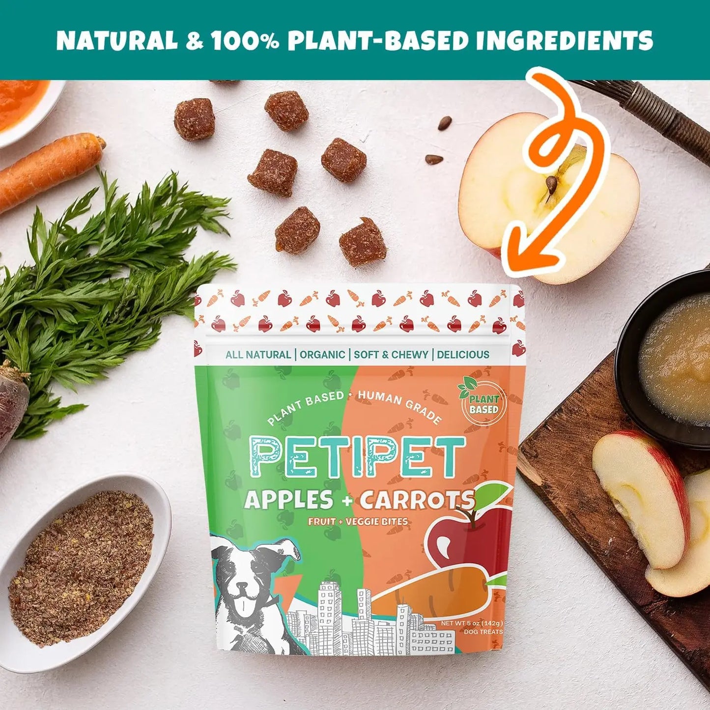 A bag of PETIPET Apples + Carrots Bites Soft & Chewy Dog Treats 5 oz sits on a table with fresh apples, carrots, and applesauce. Text: Natural, eco-friendly & 100% plant-based ingredients. Brand: PETIPET.
