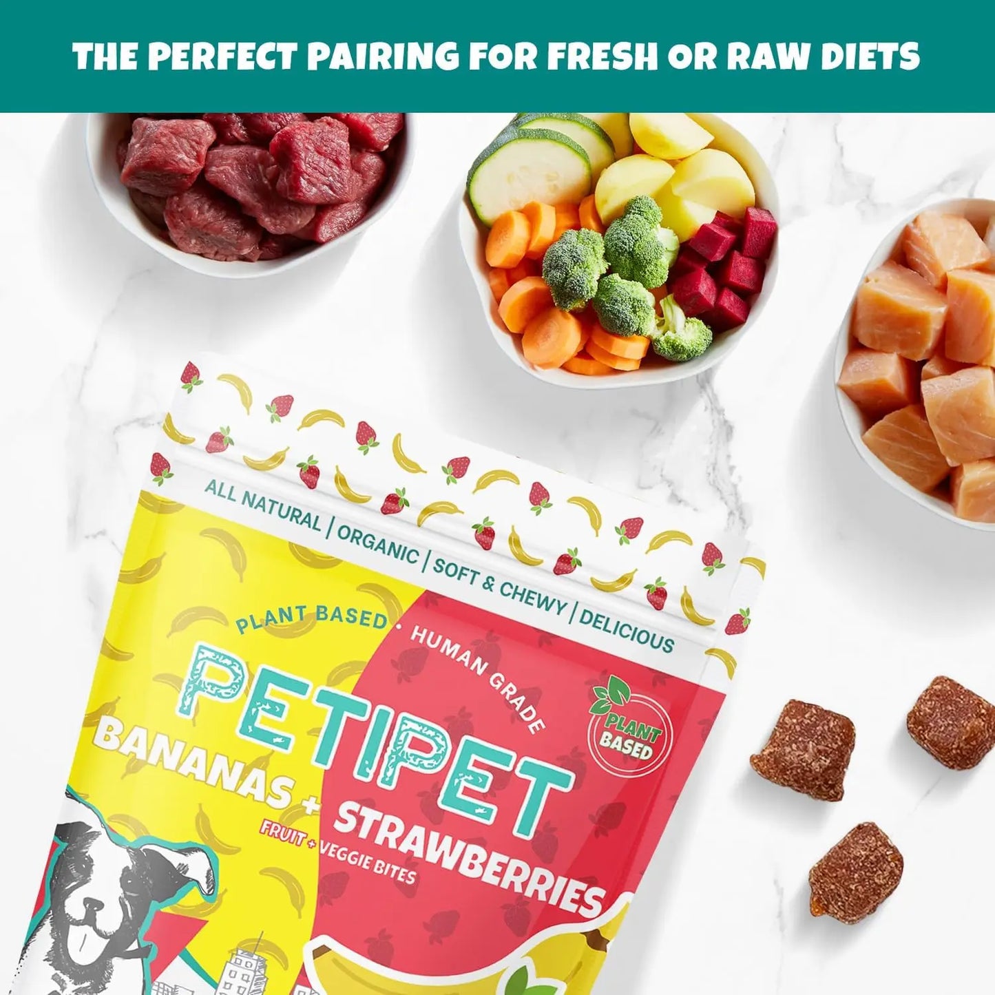 A 5 oz package of PETIPET Bananas + Strawberries Bites Soft & Chewy Dog Treats sits on a white surface, surrounded by bowls of raw meat and veggies—a perfect organic treat to pair with fresh or raw diets.