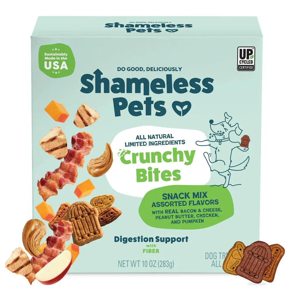 A teal 10oz box of Shameless Pets Crunchy Bites Snack Mix dog treats features assorted shapes and bacon & cheese flavors. The packaging highlights upcycled ingredients and supports digestive health.