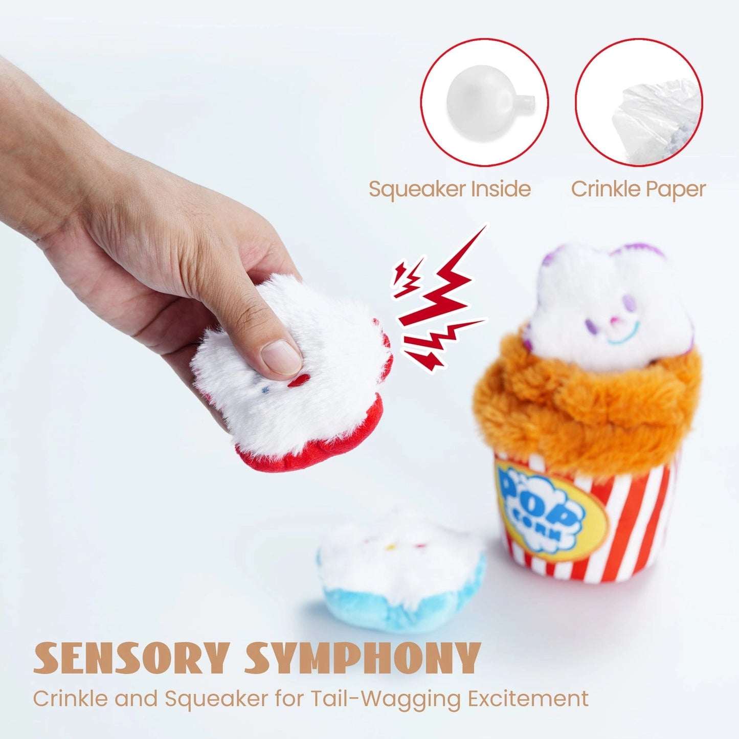 A hand squeezes the Nocciola Interactive Popcorn Bucket Dog Toy, revealing its squeaky plush and crinkle paper features. The Nocciola toy, resembling a striped popcorn bucket, sits alongside another on a white surface.