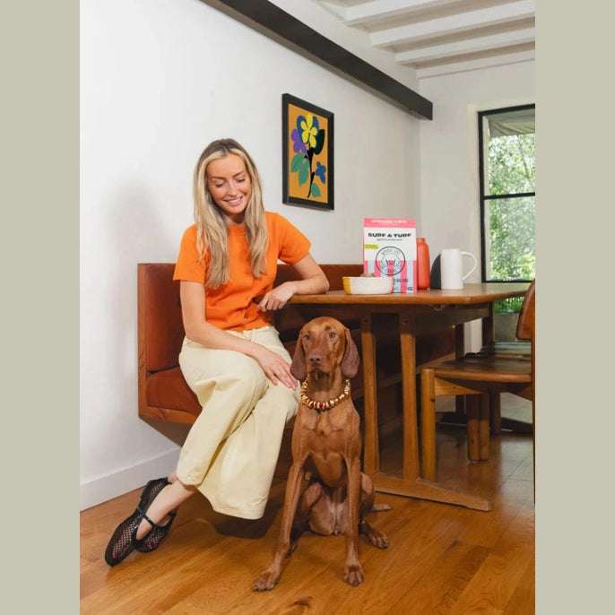Winnie Lou air dried dog food surf and turf with a happy dog sitting beside its owner in a cozy home setting