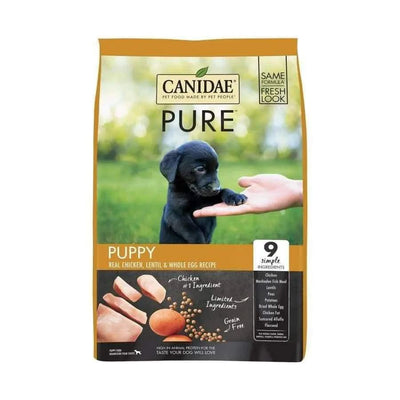 A bag of CANIDAE PURE Grain-Free Puppy Real Chicken, Lentil & Whole Egg Recipe Dry Dog Food shows a black puppy touching a person’s hand. This limited-ingredient recipe is grain-free and features chicken as the first of only 9 simple ingredients.