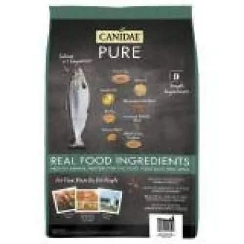 A black bag of CANIDAE PURE with Wholesome Grains Real Salmon & Barley Recipe Dry Dog Food features fish art, ingredient images, and text highlighting real food ingredients, accented with green and yellow.