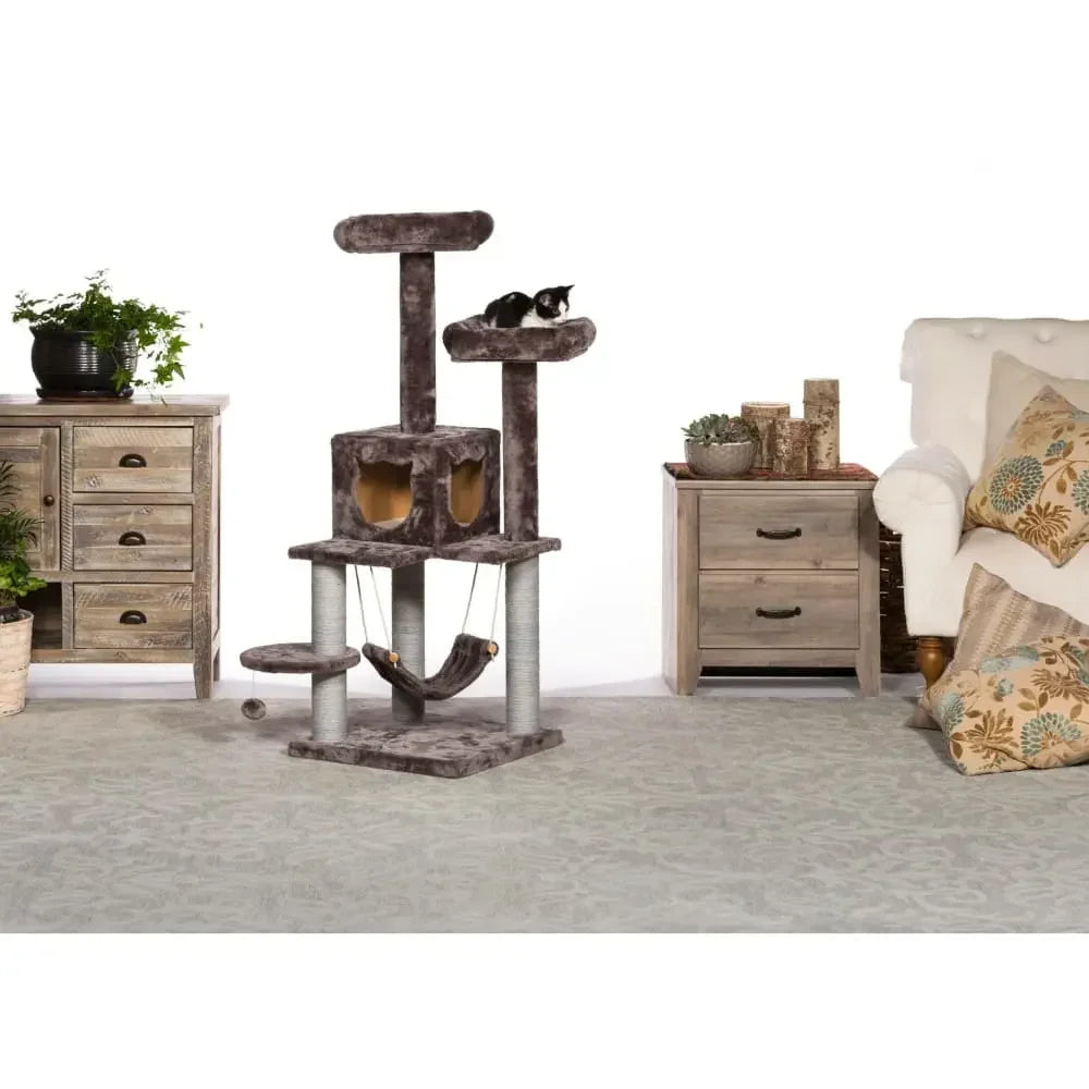 The Prevue Pet Products Kitty Power Paws Plush Party Tower—a gray cat tree with platforms, condos, scratching posts, and a hammock—stands in a living room; a black and white cat lounges on an upper platform.