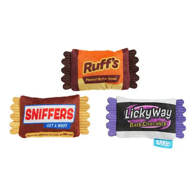 The BARK Howl-O-Ween Candy Plush Dog Toy set features three colorful, wavy-edged plush toys—Ruffs Peanut Butter Bowl, Sniffers Get a Whiff, and LickyWay Bark Choclick—each hiding a squeaky toy inside for extra fun.