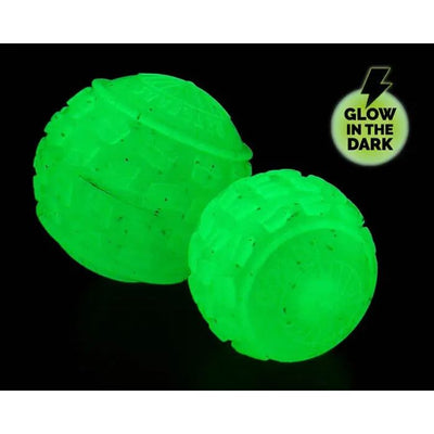 Two textured, round balls glow bright green in darkness, marked with a Glow in the Dark label and lightning bolt. Set against a black background, its the eco-friendly Cycle Dog High Roller Dog Ball - Glow in the Dark by Cycle Dog.