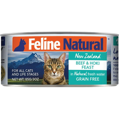A can of Feline Natural Beef & Hoki Feast Grain-Free Canned Cat Food shows a tabby cat with mountains behind and reads: New Zealand Grass-Fed Beef & Hoki Feast, in natural fresh water, for all cats and life stages. Net Wt. 85g/3oz.