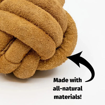 Close-up of the HuggleHounds HuggleHide Natural Leather Ball Dog Toy, featuring brown, suede-like natural leather with a black arrow and text: Made with all-natural materials! on a white background.