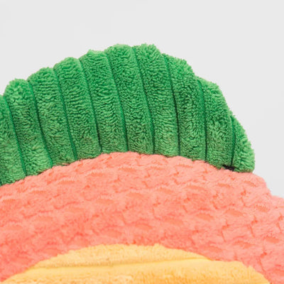 Close-up of the HuggleHounds Raucous Rainbow Trout Knottie Tough Squeaky Plush Dog Toy, featuring a textured, durable design in green, pink, and yellow leaf-like sections on a soft surface against a plain light background.
