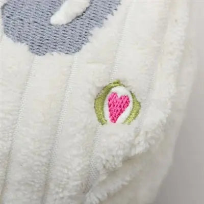 Close-up of the soft, white ribbed fabric on the HuggleHounds Shining Collection Dreidel Durable Plush Dog Toy, featuring a small embroidered pink heart outlined in green and white, with part of a gray shape above.