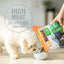 A small white dog eats from a bowl as a person pours out K9 Natural New Zealand Chicken Feast Grain-Free Freeze-Dried Dog Food, which highlights high meat content, low carbohydrate, and delicious New Zealand chicken on its packaging.