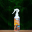 An 8oz bottle of Mad About Organics Detangler Spray for pets sits on a wooden surface with green fern leaves in the background. This natural dog conditioner features a fresh cedarwood scent and a label with a dog and American flag.