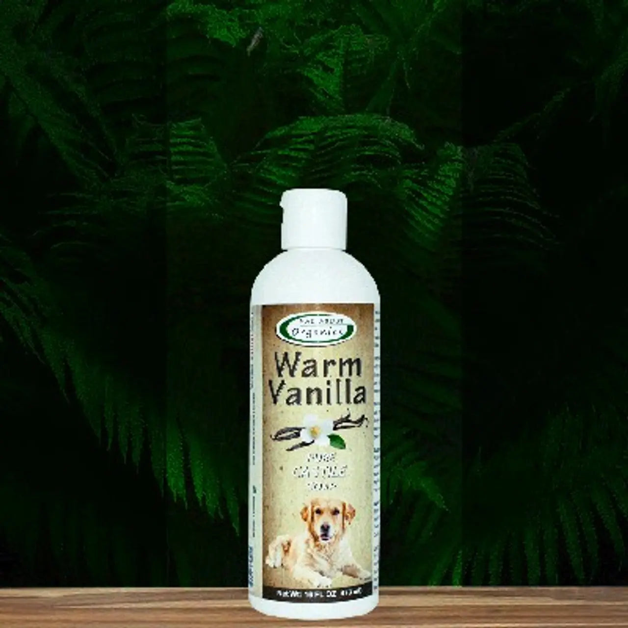 A 16oz bottle of Mad About Organics Warm Vanilla Dog Shampoo for sensitive skin, made with organic ingredients, features a dog on the label and is set against green fern leaves.