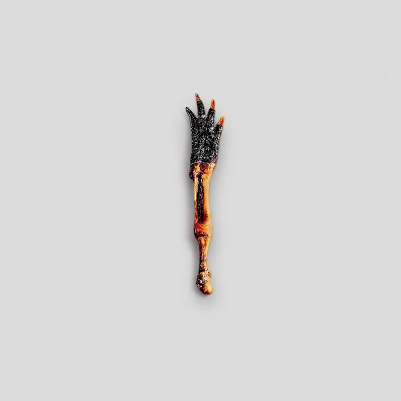 A single Nutrigator® Farm-Raised Alligator Foot Hypoallergenic Dog Treat from Mosaic, with blackened skin and visible bone, is centered on a plain light gray background—showcasing this unique bulk dog treat.