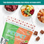 A 5 oz bag of PETIPET Apples + Carrots Bites Soft & Chewy Dog Treats is shown on a marble surface among bowls of veggies, fruit, and meat. These eco-friendly, plant-based treats are perfect for fresh or raw diets.