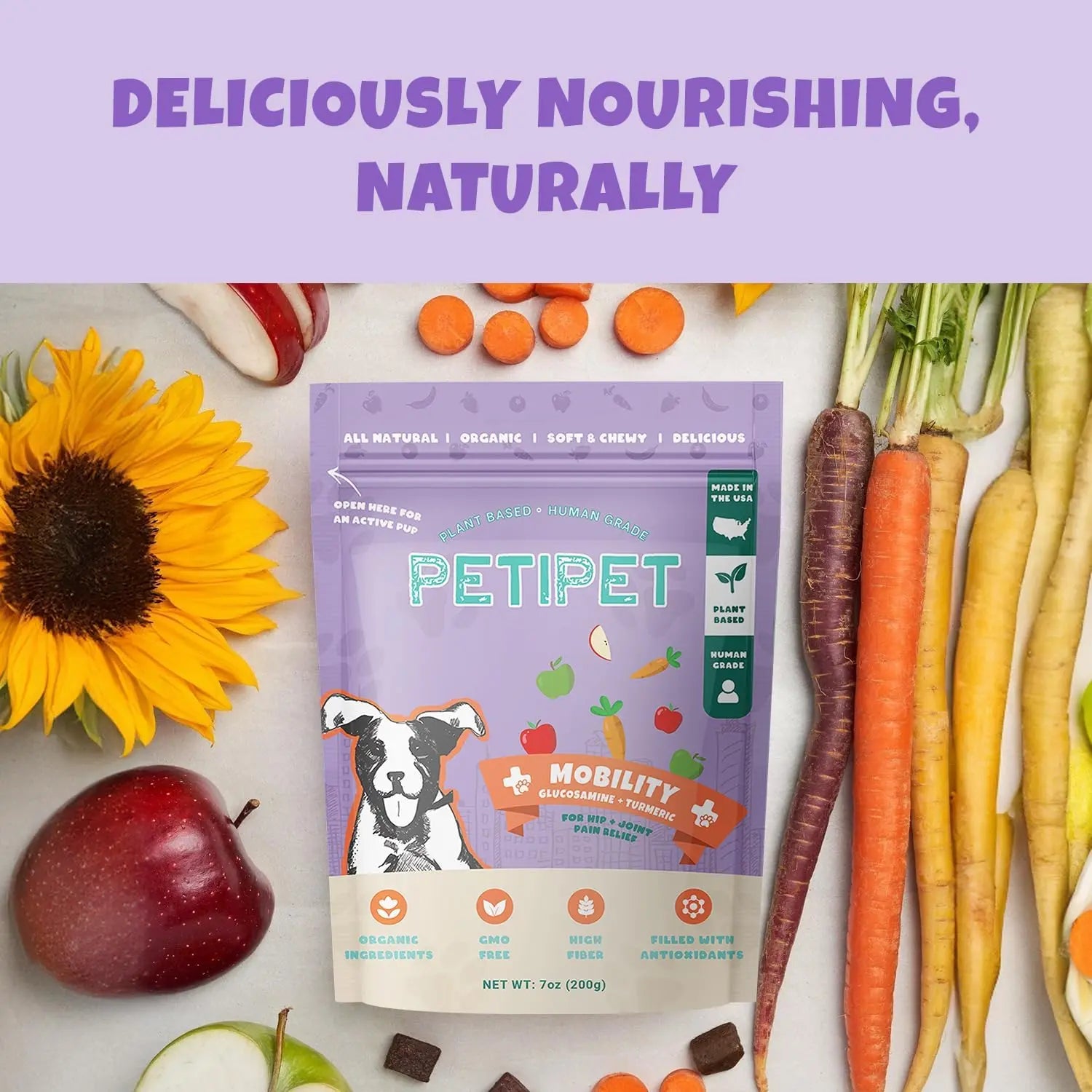 A 7oz bag of PETIPET Mobility Bites with Glucosamine + Turmeric Apple & Carrot Flavored Soft Chews for dogs sits on a yellow plate with carrots, a sunflower, and an apple. Above, “Deliciously Nourishing, Naturally” is shown on a purple background.