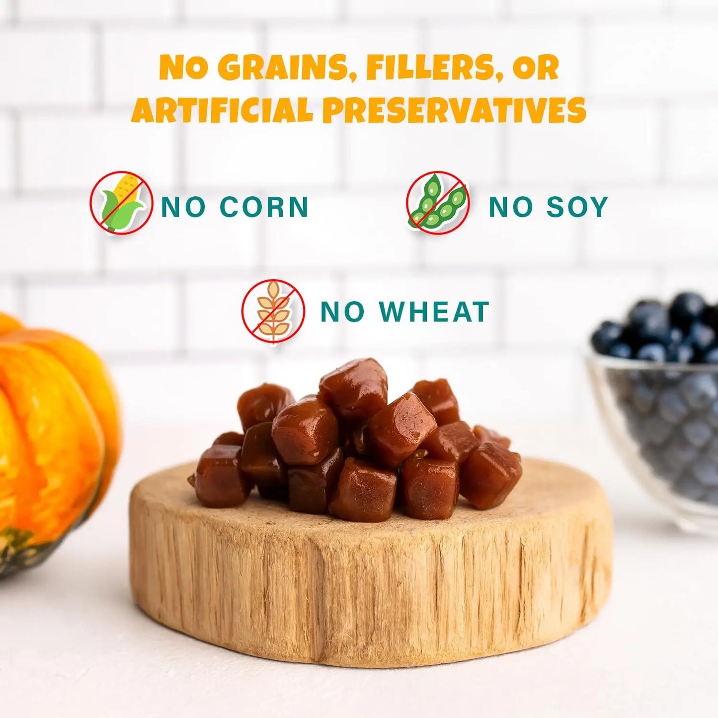 A pile of chewy brown treats rests on a wooden board, near a pumpkin and blueberries. Text reads: No grains, fillers, or artificial preservatives. PETIPET Pumpkin Fruit + Veggie Bites—Gluten-Free Vegan Dog Treats you can trust.