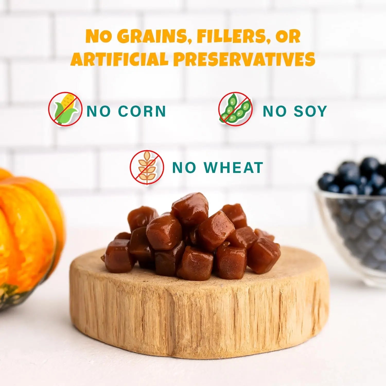 A pile of chewy brown treats rests on a wooden board, near a pumpkin and blueberries. Text reads: No grains, fillers, or artificial preservatives. PETIPET Pumpkin Fruit + Veggie Bites—Gluten-Free Vegan Dog Treats you can trust.