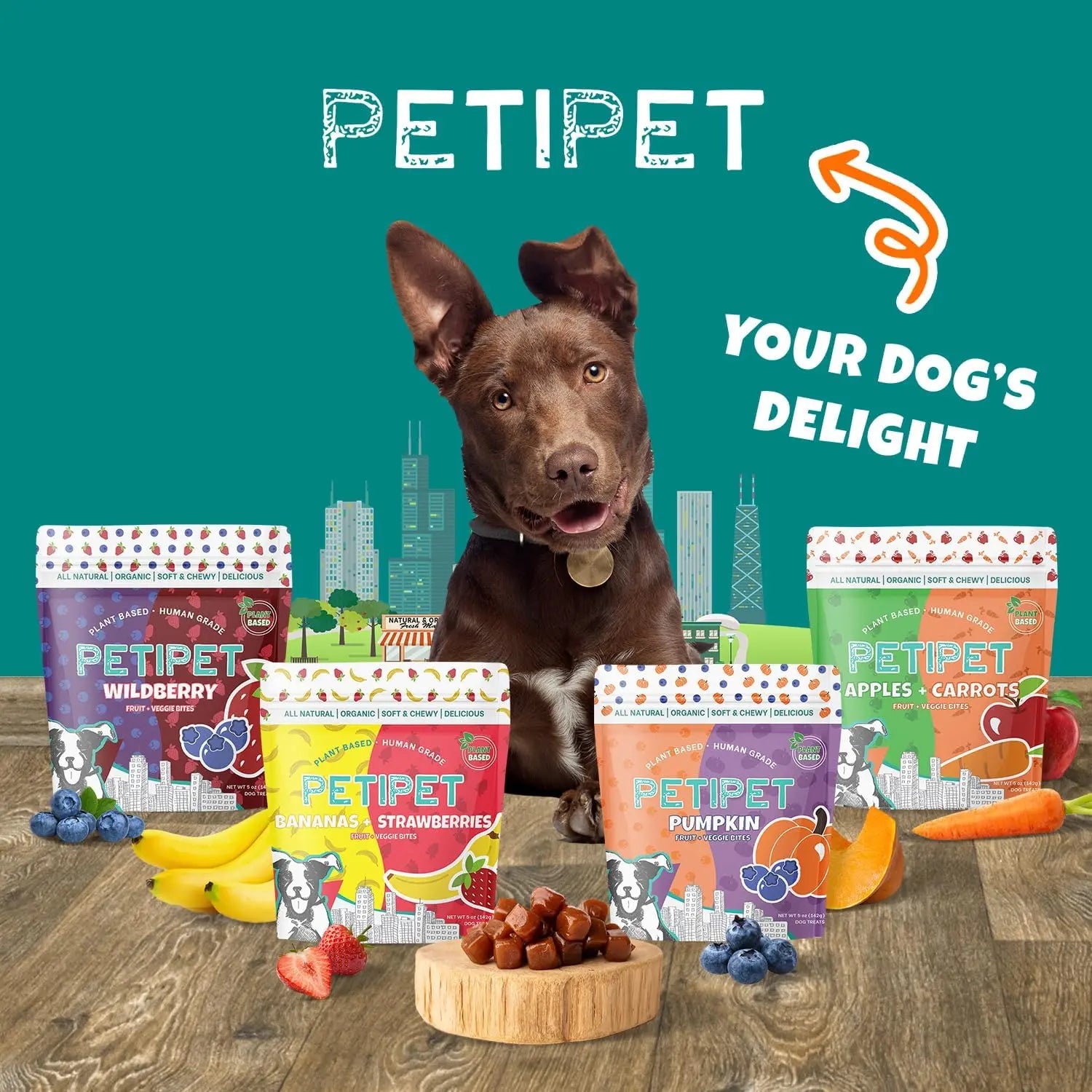 A happy brown dog sits behind four bags of PETIPET Pumpkin Fruit + Veggie Bites Gluten-Free Adult Soft & Chewy Dog Treats—made with human-grade ingredients and surrounded by fresh produce. Text reads PETIPET Your Dogs Delight.