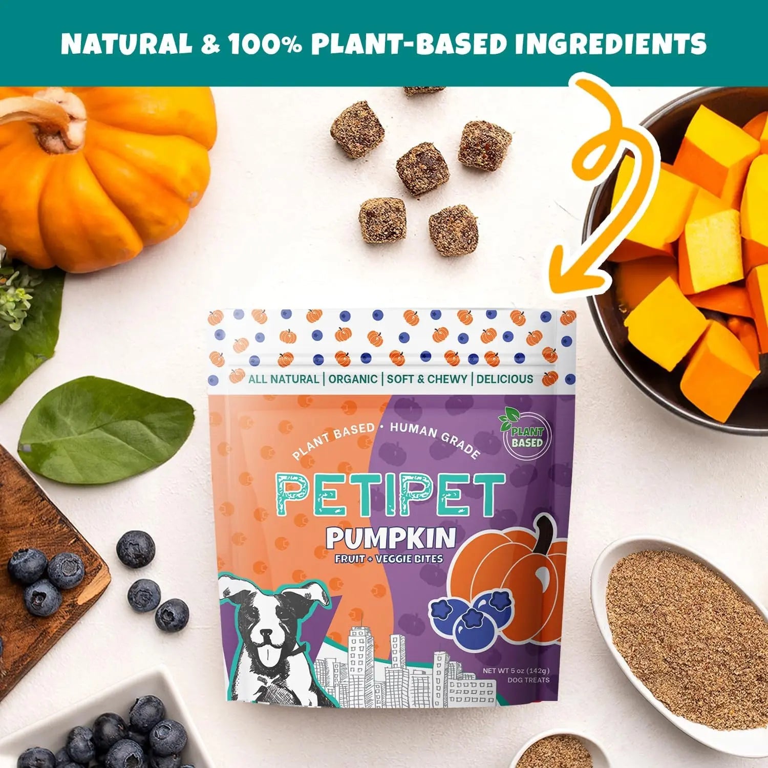 A bag of PETIPET Pumpkin Fruit + Veggie Bites Gluten-Free Adult Soft & Chewy Dog Treats 5oz sits on a white surface with blueberries, pumpkin, sweet potato pieces, and grains. A banner above reads: Natural, 100% Plant-Based, Vegan, Human-Grade Ingredients.