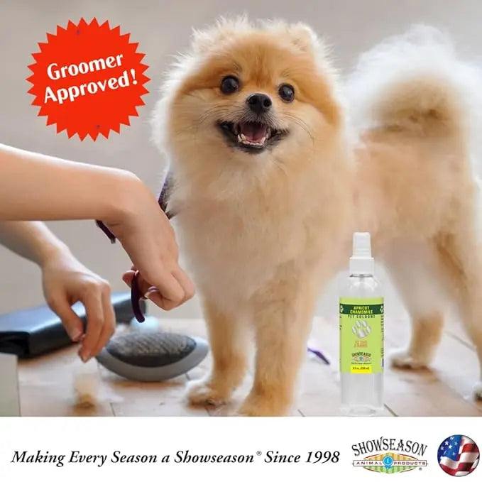 A small, fluffy dog is groomed on a table as hands hold scissors and a brush. Cruelty-free Showseason Spring Rain Dog Cologne and a spray bottle sit nearby. A red Groomer Approved! badge and brand logos are shown at the bottom.