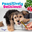 A small, fluffy puppy bites a green Woof Island Smoked Kalua Pork Rolls chew while lying in a gray pet bed. Text above reads Pawsitively Delicious! with colorful leaves. A hand holds the treat; Woof Island logo is in the corner.