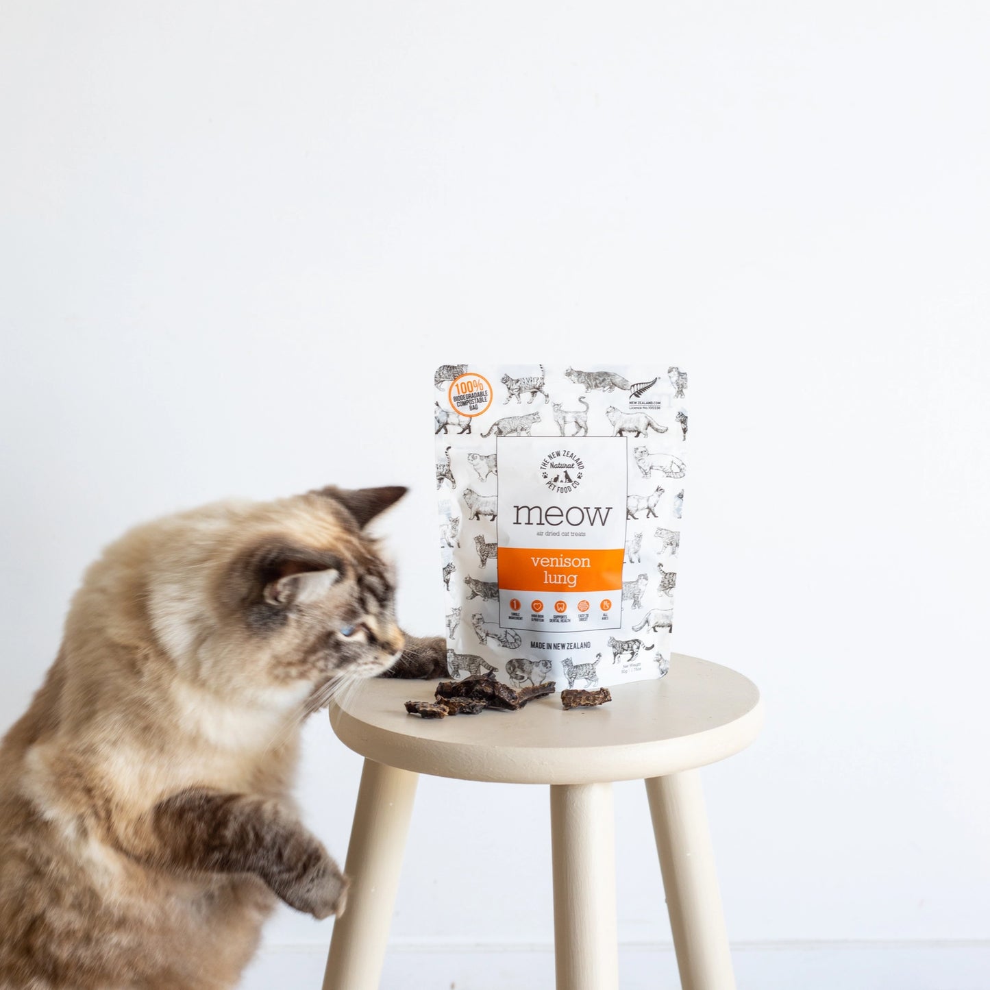 The New Zealand Natural Pet Food Co venison lung cat treats bag with a playful cat on a stool