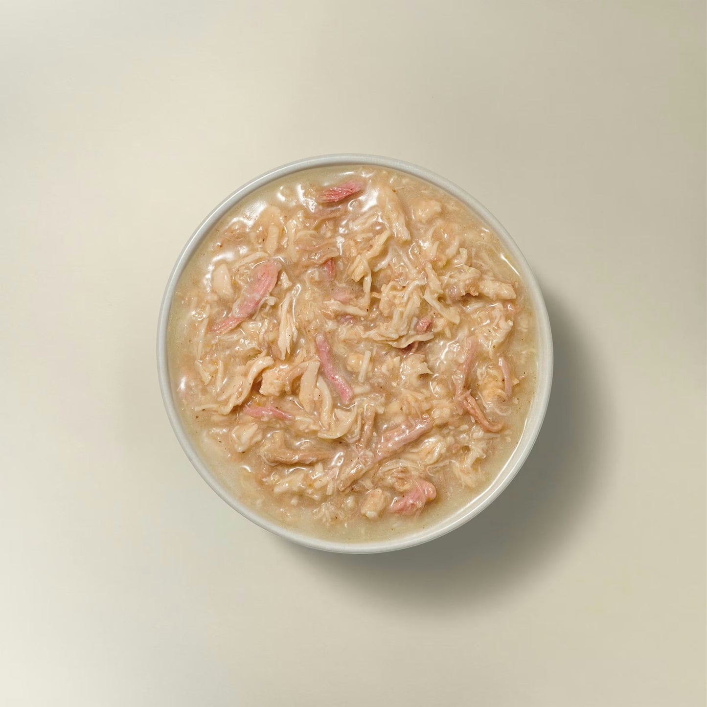 Petcurean grain free wet cat food in a bowl featuring shredded meat and a savory broth