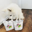 White dog beside two bags of freeze dried duck dog food from The New Zealand Natural Pet Food Co